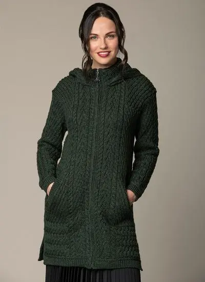 smiling brown haired woman wearing a dark green aran knitted coatigan with hands in pockets